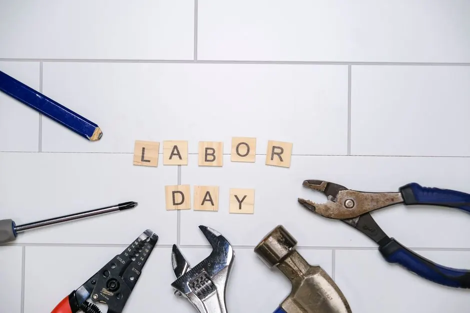 Flat lay of tools and Labor Day text on white tiles, symbolizing construction and work theme.